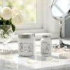 PACK ANTI-ÂGE : pot et flacon blancs sur une surface miroir, ambiance lumineuse avec roses et miroir de beauté en arrière-plan.